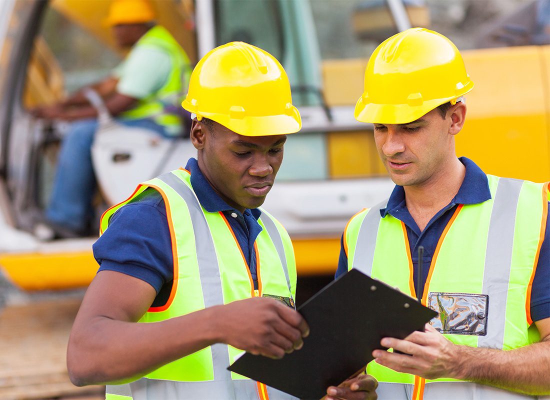 Employee Benefits - Construction Workers Discussing Work Plan With a Construction Vehicle in the Background