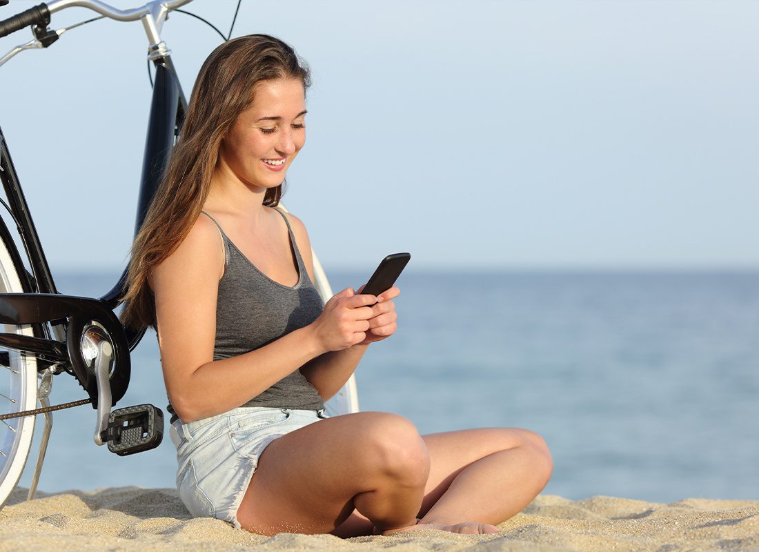 Read Our Reviews - Woman Smiling at Phone While Leaning Against Her Bicycle on the Beach